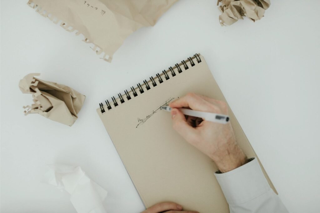 A frustrated artist’s hand scratching out a drawing in a sketchbook, surrounded by crumpled paper — a visual of creative burnout and an art slump.