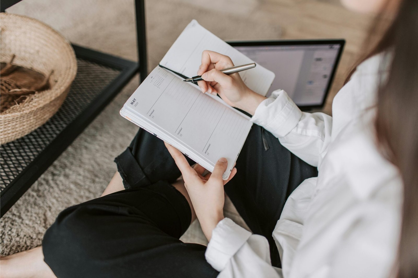 Artist planning her daily art routine with a planner and laptop on the floor.