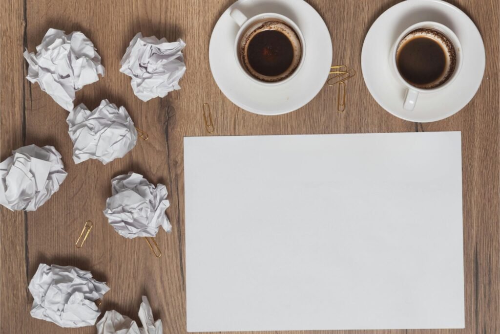 Blank sheet of paper surrounded by crumpled papers and coffee mugs, symbolizing struggles with starting an art routine.